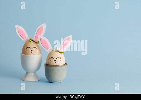 Cute Easter bunny shaped eggs in egg holders on blue background. Place for your text Stock Photo