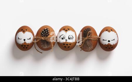Funny owl family. Brown Easter eggs with painted faces, eggs with bird feathers. Stock Photo