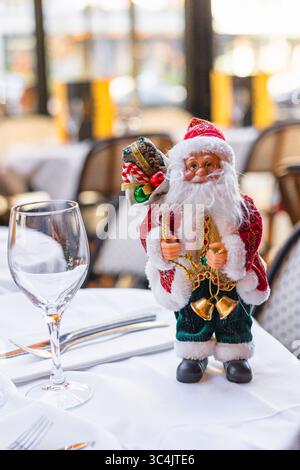 A decorative Santa Claus figurine stands on a table. The Santa has a red suit, white beard, and holds gifts. A wine glass is placed beside him. Stock Photo