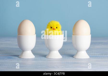 Minimalist Easter composition with plush chicken and eggs in cups on pastel blue background Stock Photo