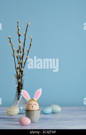 Easter bunny eggs in egg holder on blue background. Multicolored eggs and sprigs of willow. Place for your text Stock Photo