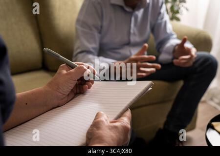 High contrast, cinematic shot of a man gesturing during a difficult emotional confession to his therapist, who is taking notes in a dark room. Stock Photo