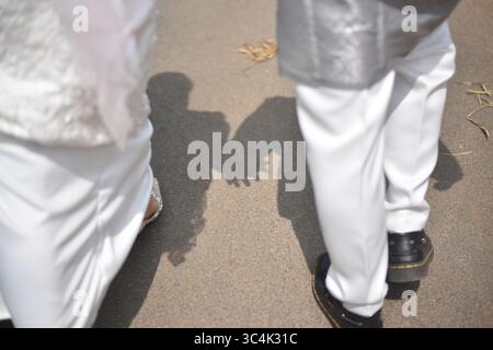 A close-up image showing two people holding hands in sunlight, casting shadows on the pavement, symbolizing connection and unity Stock Photo