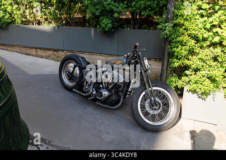 A vintage custom motorcycle, parked on a city street, basks in sunlight.  Its metallic grey finish and large tires create a cool, urban aesthetic. Ide Stock Photo