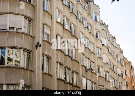 A striking low-angle shot of a tan Art Deco apartment building, featuring repeating curved bay windows and white window frames.  The image evokes a se Stock Photo