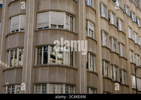 A detailed close-up of a tan Art Deco building's facade, featuring numerous bay windows with white frames and partially closed blinds.  The image evok Stock Photo