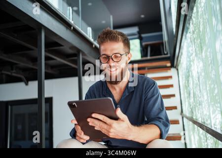 A young man focuses on his tablet in a modern, stylish workspace designed for innovation Stock Photo