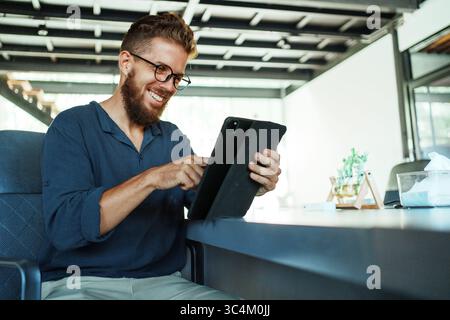 A focused young man is engaging with a tablet in a stylish and modern contemporary office setting Stock Photo