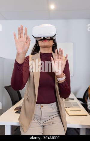 Woman wearing VR headset interacting with virtual interface at meeting table with laptop Stock Photo