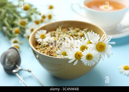 Chamomile flowers in bowl on light blue background, closeup Stock Photo