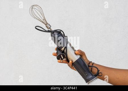 Close-up of a female hand grasping a grungy old electric hand blender. Visible dust and surface scratches on its body. Perfect for retro, worn, and ag Stock Photo