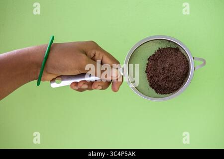 Female hand displaying tea leaves in a steel strainer. Used tea granules are a natural fertilizer, perfect for sustainable plant care and composting. Stock Photo