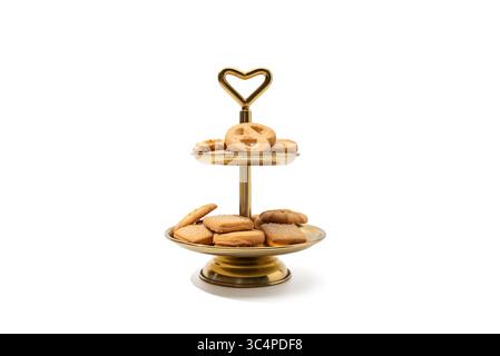 Cookies on Gold Cake Stand White Background. Danish butter cookies are elegantly displayed on a two tier golden tray with a heart-shaped handle. The a Stock Photo