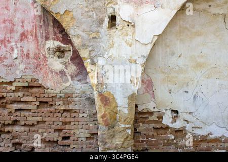 Close-up of an old weathered wall showing layers of exposed brick, crumbling plaster, and faded paint. The surface reveals textures and natural colors Stock Photo