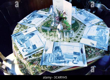 Placemat restaurant Flora, Hoofddorp, The Netherlands, 31-05-1997 Whizgle News, Dutch Desk, The Netherlands, 1950-2000 A cozy dining setup features a round table elegantly decorated with a patterned tablecloth, surrounded by wooden chairs. Each place setting showcases a unique menu and a striking blue-toned image of a person enjoying a drink, creating a nostalgic atmosphere. A small vase with fresh flowers adds a touch of color to the table, enhancing its inviting appeal. Stock Photo