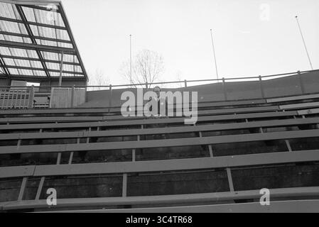 Harmen de Roos, football crazy, 26-03-1991 Whizgle News, Dutch Desk, The Netherlands, 1950-2000 A solitary figure sits quietly on empty stadium bleachers, surrounded by an expansive, open space. The starkness of the setting emphasizes a sense of solitude, with a few trees visible in the background. Stock Photo
