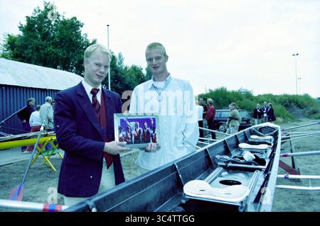 Honoring rower Paul de Jong, silver at the 2003 World Championships in Milan., Haarlem, The Netherlands, 06-09-2003 Whizgle News, Dutch Desk, The Netherlands, 1950-2000 Two young men stand by a rowing boat, one proudly holding a framed photo, while the other wears a medal around his neck. In the background, people gather near the water, creating a lively atmosphere. The scene suggests a celebration or award ceremony related to a rowing event. Stock Photo