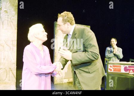 Henny Orrie Theater Haarlem, Haarlem, Wilsonsplein, The Netherlands, 12-12-2002 Whizgle News, Dutch Desk, The Netherlands, 1950-2000 A moment of celebration as an older woman graciously receives an award from a man in a suit, while another individual in the background watches with a smile. The scene captures a heartfelt exchange filled with appreciation and recognition. Stock Photo