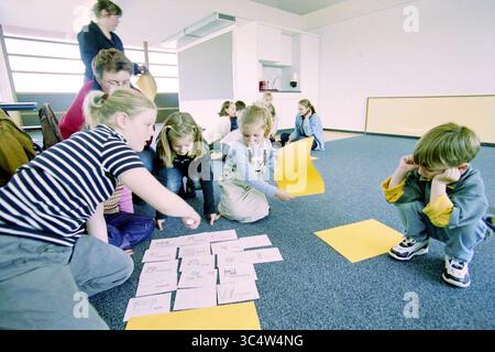 Participation afternoon, Nieuw-Vennep, 17-04-2001 Whizgle News, Dutch Desk, The Netherlands, 1950-2000 A group of children is engaged in a collaborative activity on the floor, studying sheets of paper that outline various drawings. Some are pointing at the papers while others observe thoughtfully, contributing to the creative process in a classroom setting. An adult oversees the activity, fostering an atmosphere of learning and exploration. Stock Photo