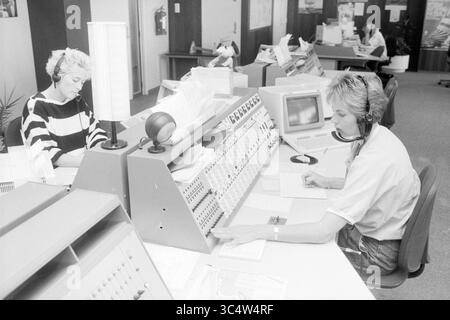 Telephone operator Radio Scheveningen IJmuiden, radio, telephone, telephony, IJmuiden, The Netherlands, 03-08-1988 Whizgle News, Dutch Desk, The Netherlands, 1950-2000 Two operators work at a busy call center, each focused on their tasks. One is taking notes while the other manages a console filled with buttons and controls, both connected with headsets. The environment reflects a professional, organized workspace designed for communication. Stock Photo
