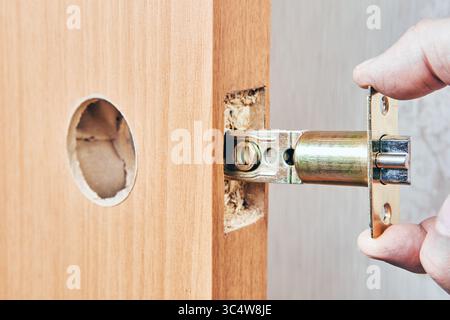 Latch mechanism being inserted into precut hole on door edge aligning with round bore for further knob installation and locking function. Stock Photo