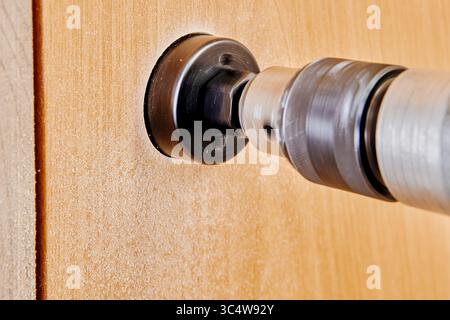 Saw cup installed on cordless drill preparing to bore opening for latch in wooden interior door photographed from lower frontal angle. Stock Photo