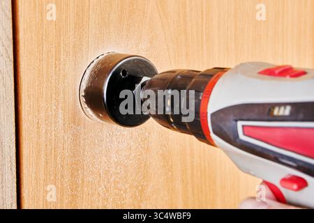 Drill cutter held in hands of tradesman during boring operation into edge of interior wooden door captured from medium low perspective. Stock Photo