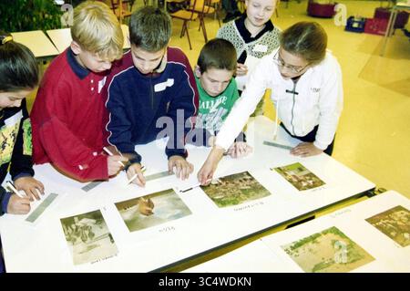 Most beautiful photo in the newspaper, Haarlem, The Netherlands, 24-11-1998 Whizgle News, Dutch Desk, The Netherlands, 1950-2000 A group of children is engaged in a classroom activity, examining various images laid out on a table while taking notes. They appear focused and collaborative as they discuss and analyze the pictures. Stock Photo
