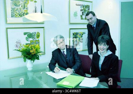 Lawyer Niek Pesman, Haarlem, The Netherlands, 12-01-1999 Whizgle News, Dutch Desk, The Netherlands, 1950-2000 A group of three professionals is gathered around a glass table in a modern office setting, engaged in a discussion. One man is seated, signing documents, while a woman smiles and poses next to him. A third man stands behind, looking on. Vibrant artwork adorns the walls, adding a colorful backdrop to the scene. A vase of flowers adds a touch of warmth to the environment. Stock Photo