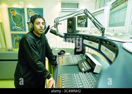 Radio station, Hoofddorp, The Netherlands, 04-12-2001 Whizgle News, Dutch Desk, The Netherlands, 1950-2000 A young man stands confidently at a radio studio mixing desk, wearing headphones and speaking into a microphone. Behind him, monitors display sound levels and audio tracks, while promotional posters adorn the walls, creating a vibrant atmosphere of creativity and music. Stock Photo