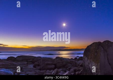 March 31, 2017 - Australia - The waxing crescent Moon in deep evening twilight with stars beginning to appear, with the Moon in Taurus above the Pleiades cluster at right and below the Hyades and Aldebaran above. This was March 31, 2017 from Cape Conran, West Cape area, on the Gippsland Coast of Victoria, Australia. The Moon looks turned around from what we are used to seeing it in the northern hemisphere in the evening sky. ..This is a stack of 8 exposures, mean combined to smooth noise, for the ground and one exposure for the sky. An added Orton Effect gaussian blur layer adds the dreamy sof Stock Photo