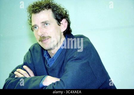 Mr. Warmerdam, ID Expo, IJmuiden, IJmuiden, The Netherlands, 25-03-1999 Whizgle News, Dutch Desk, The Netherlands, 1950-2000 A man with curly hair and a mustache rests his arms on a table, appearing thoughtful and engaged in conversation. He is dressed casually in a sweater and collared shirt, exuding a relaxed yet attentive demeanor. Stock Photo