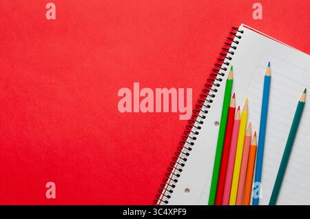 A notebook and some colorful pencils on red background and copy space. Back to school concept. Stock Photo