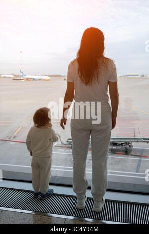 Mother and child watching airplane taking off from airport window Stock Photo
