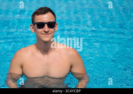 Young man relaxing in swimming pool wearing sunglasses Stock Photo