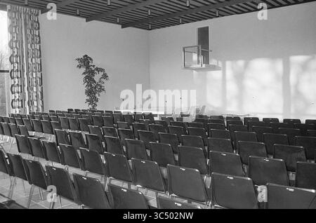 Interior Council Chamber etc. new Heemstede Town Hall., Heemstede Municipal Council, 10-12-1973 Whizgle News, Dutch Desk, The Netherlands, 1950-2000 A spacious conference room featuring rows of dark chairs arranged neatly facing a minimalist table. Large windows allow natural light to illuminate the space, with a potted plant adding a touch of greenery in the corner. The modern architecture is characterized by clean lines and an open atmosphere. Stock Photo