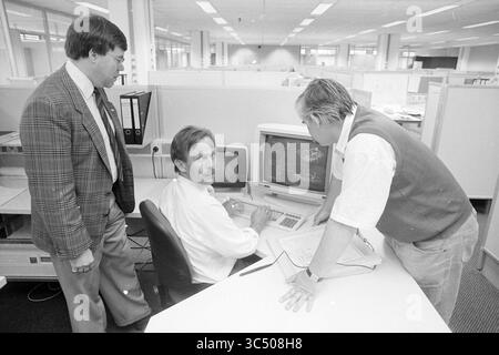 Employee(s) Fluor, Schalkwijk, Haarlem, Nederland, 07-05-1990 Whizgle News, Dutch Desk, The Netherlands, 1950-2000 Three professionals engage in a discussion at a workspace. One sits at a computer, analyzing data on the screen, while the others stand nearby, leaning in to offer insights and feedback. The office setting features cubicles and a collaborative atmosphere. Stock Photo