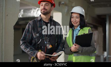 Asian female engineer Caucasian male worker handshake site inspection discussion construction teamwork partnership safety planning shake hands Stock Photo