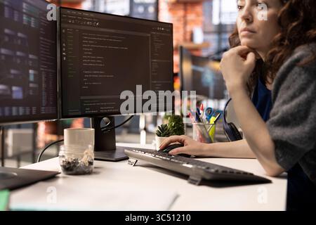 Female programmer seen typing code for a user interface design on dual monitors, working in a digital workspace. Woman IT specialist working on software engineering and front end development. Stock Photo