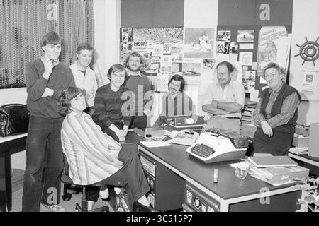 Hans Bongers + group photo ed. IJC, Haarlems Dagblad etc. and IJmuider Courant and Koeri, 15-10-1980 Whizgle News, Dutch Desk, The Netherlands, 1950-2000 A diverse group of eight individuals gathers around a desk in an office setting, engaged in conversation and collaboration. The atmosphere appears lively, with various notes and posters decorating the walls, hinting at a creative environment. A typewriter sits prominently on the desk, symbolizing a focus on writing or journalism. Stock Photo