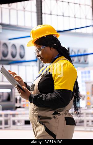 Industrial production supervisor holding tablet, tracking operational performance. Black female tech specialist using digital device, enhancing system functionality for smoother warehouse operations. Stock Photo