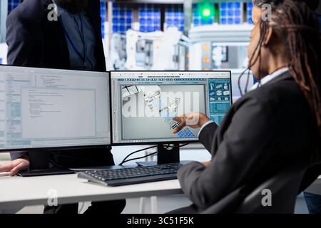 Programmer in photovoltaics factory office using PC to update software of robot arms placing solar panels on assembly lines, communicating changes to team leader, close up shot Stock Photo