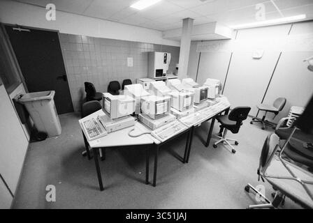 Equipment for the auction of Infotheek by Troostwijk Whizgle News, Dutch Desk, The Netherlands, 1950-2000 A cluttered workspace featuring multiple vintage computer monitors arranged on a large table, surrounded by empty chairs and an adjacent kitchenette area. The setting conveys an atmosphere reminiscent of an earlier era in technology and office design. Stock Photo