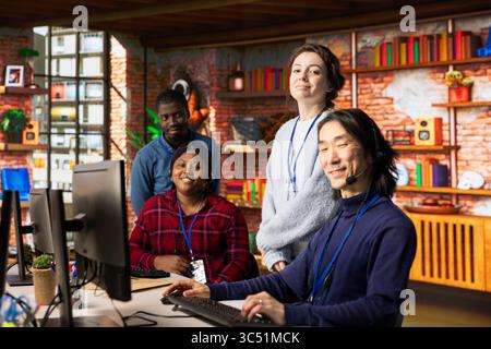 Portrait of joyful multiethnic call center agents in office providing step by step guidance to customers. Happy multiracial customer support workers at PC desk walking clients through solutions Stock Photo