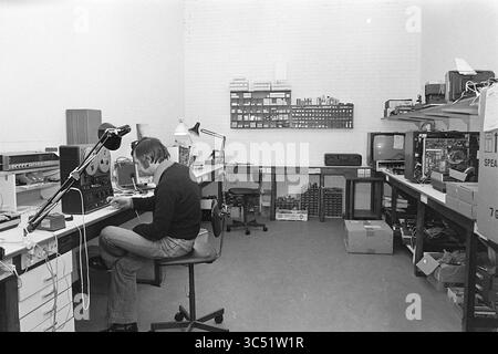 Interior and exterior Fa. Pruis IJmuiden, Shops and kiosks, 22-03-1978 Whizgle News, Dutch Desk, The Netherlands, 1950-2000 A person is focused intently on a workbench cluttered with electronic components and tools, surrounded by shelves filled with organized parts. The workspace reflects a blend of creativity and technology, showcasing a dedicated environment for tinkering and experimentation. Stock Photo