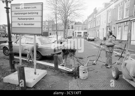 Striping project Nieuwe Kerksplein, Haarlem, Nieuwe Kerksplein, The Netherlands, 03-12-1990 Whizgle News, Dutch Desk, The Netherlands, 1950-2000 Workers are engaged in a parking project, digging and installing infrastructure while signs indicate no parking during the construction. Nearby, an old car is parked alongside residential buildings that line the street. Stock Photo