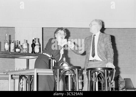Rehearsal for the elderly theater Beverwijk, Theater, Beverwijk, The Netherlands, 16-03-1987 Whizgle News, Dutch Desk, The Netherlands, 1950-2000 A woman playfully raises a glass in a toast while seated at a bar, as a man beside her smiles and leans slightly forward. Behind them, various bottles line the shelves, creating a lively atmosphere of celebration. Stock Photo