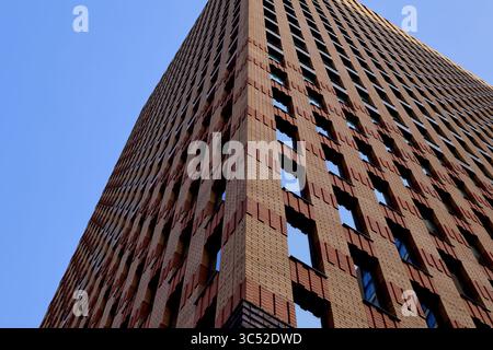 Corner view of a tall brick building in Amsterdam shows windows and textures rising into blue sky, highlighting geometric design and urban style. Stock Photo
