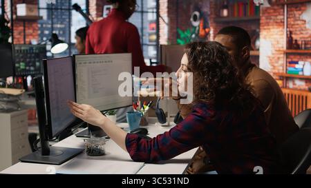 Startup programmer collaborating with colleague to test company software, identifying bottlenecks. Team of engineers writing clean, efficient code in programming language to reduce errors, camera A Stock Photo