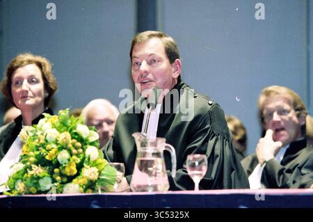 Installation of court president Mr. Baker, 07-04-1999 Whizgle News, Dutch Desk, The Netherlands, 1950-2000 A speaker in academic regalia addresses an audience, while seated individuals listen intently. A floral arrangement and a pitcher of water are present on the table in front of the speaker. Stock Photo
